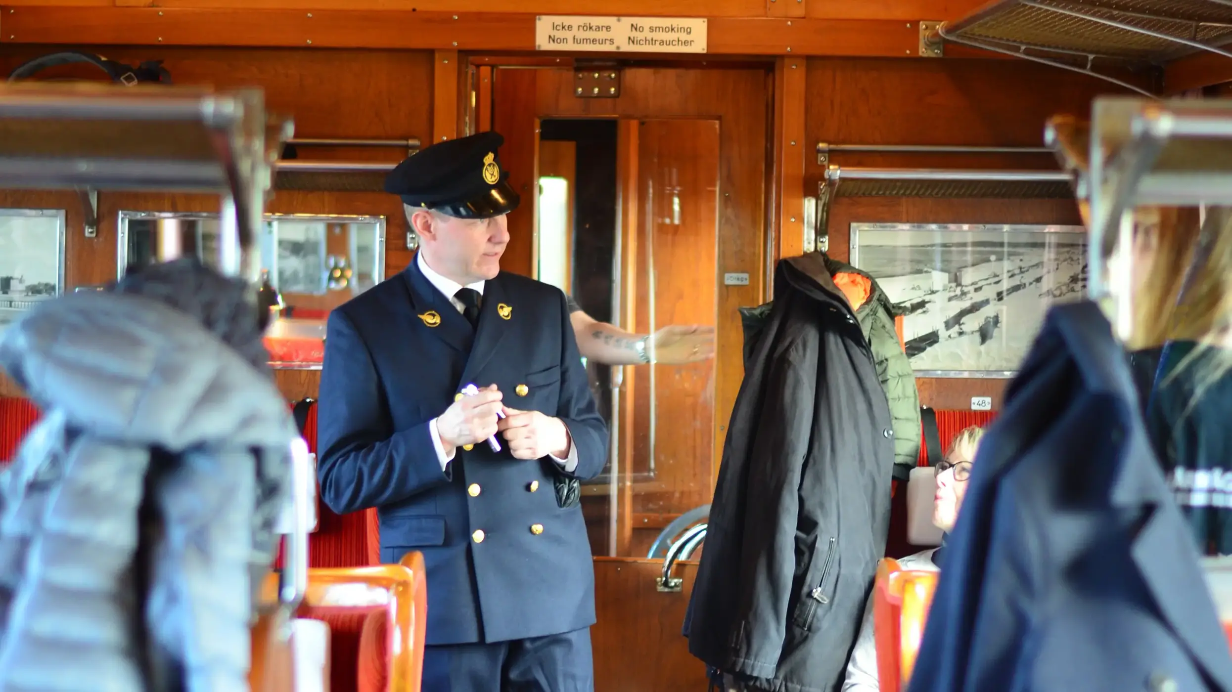 En tågkonduktör inspekterar biljetterna inne på ett historiskt gammalt tåg. Foto. 
